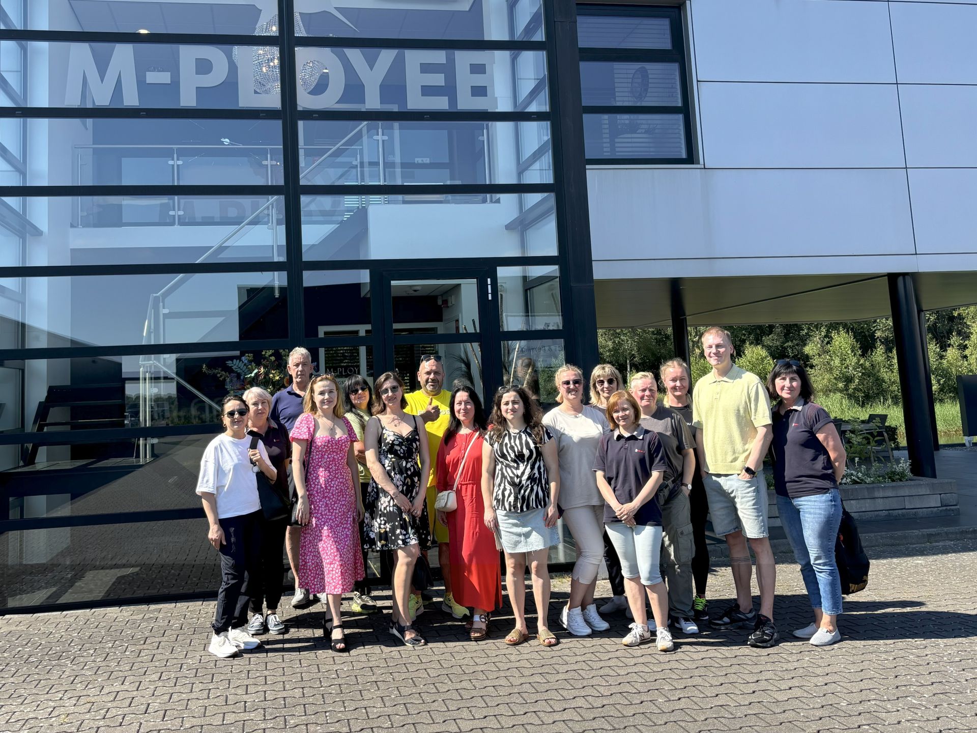 Een groep mensen poseert voor een gebouw op een zonnige dag.