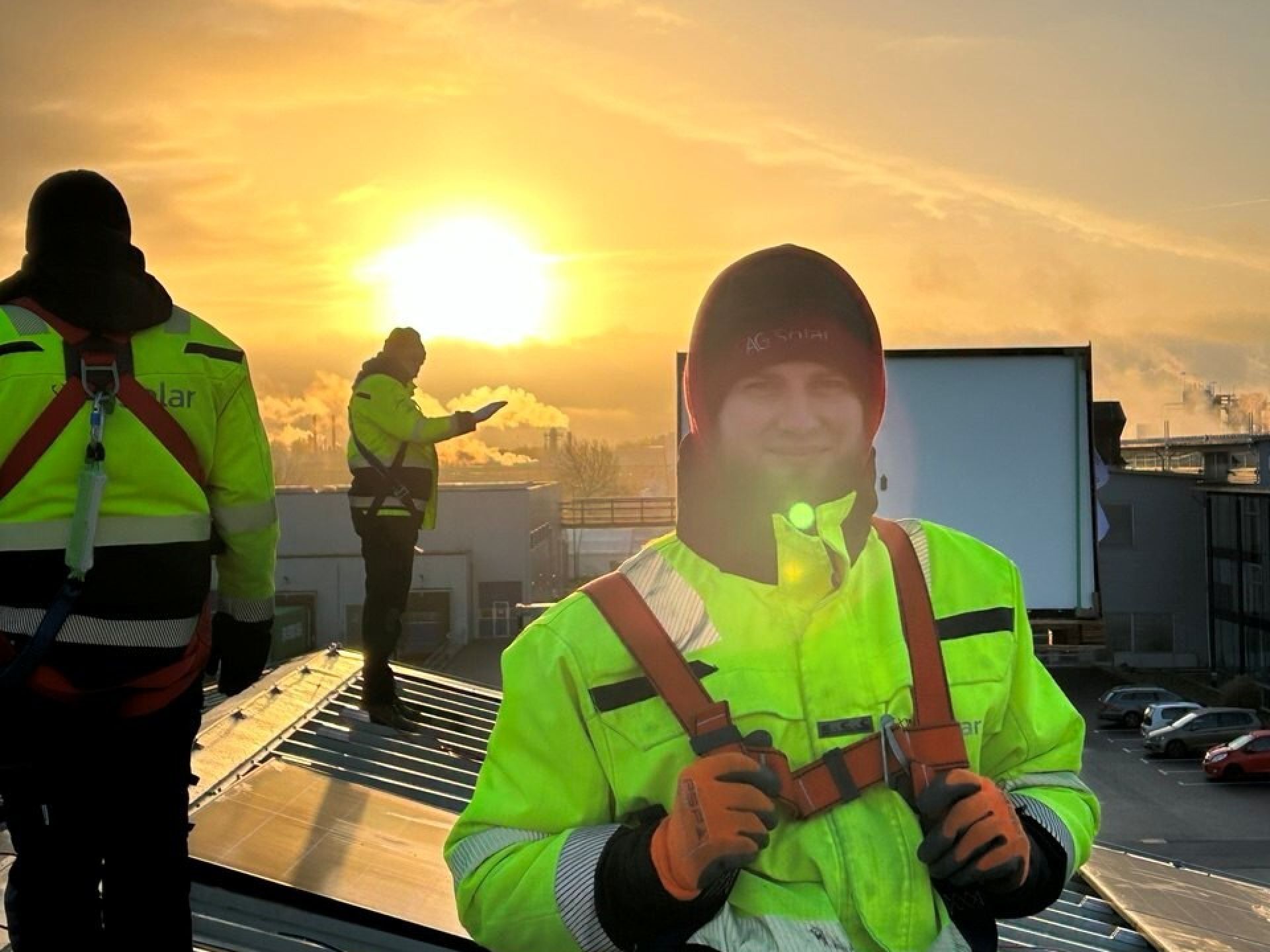 Arbeiders in veiligheidshesjes op een dak bij zonsondergang.