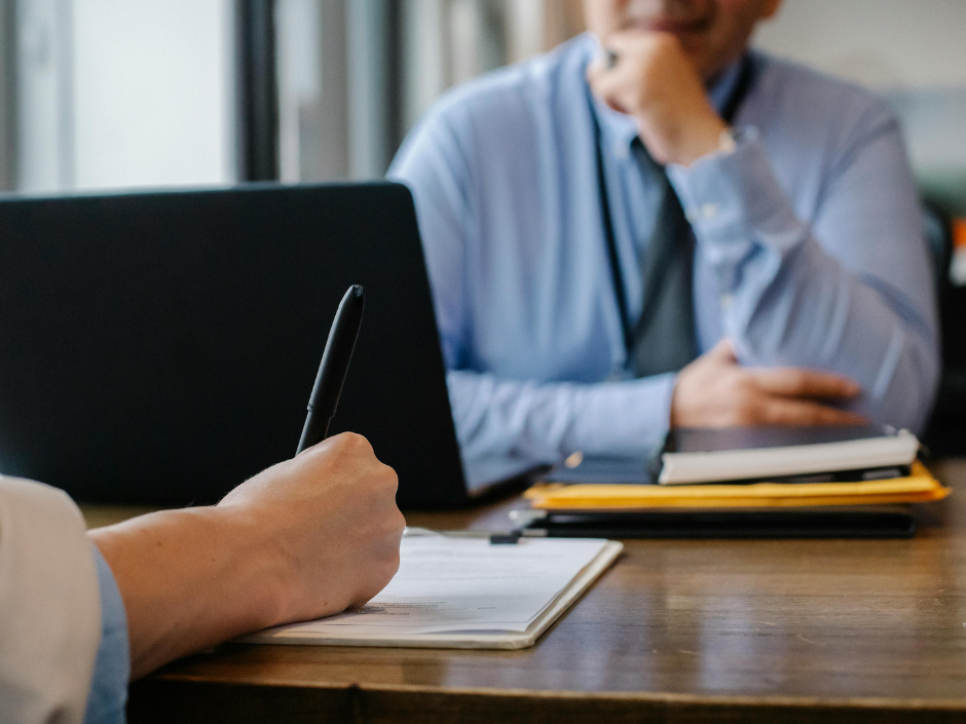 Twee personen in een zakelijke bespreking, één maakt aantekeningen.