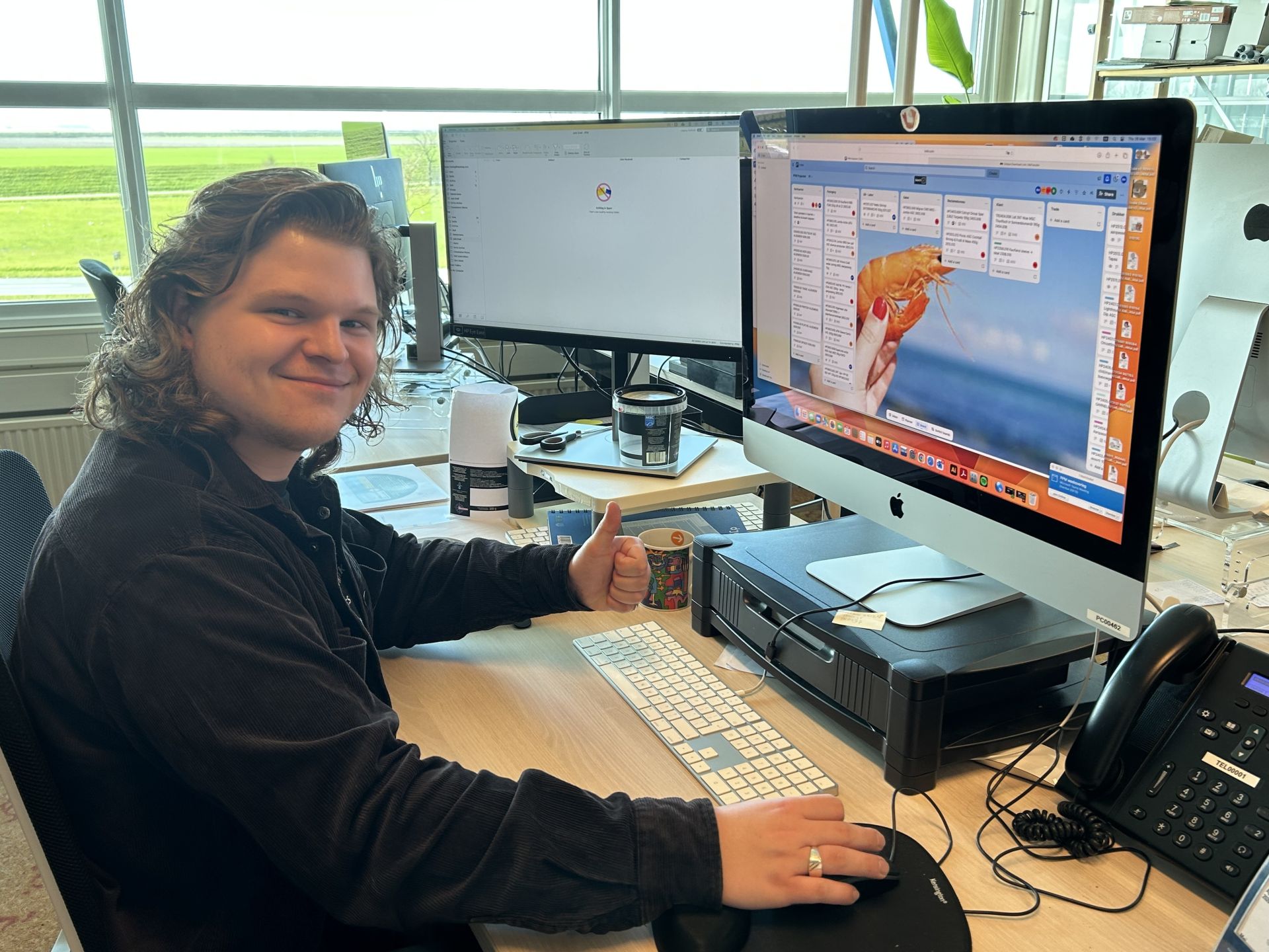 Een persoon achter een bureau geeft een duim omhoog terwijl hij naar een computerscherm kijkt.