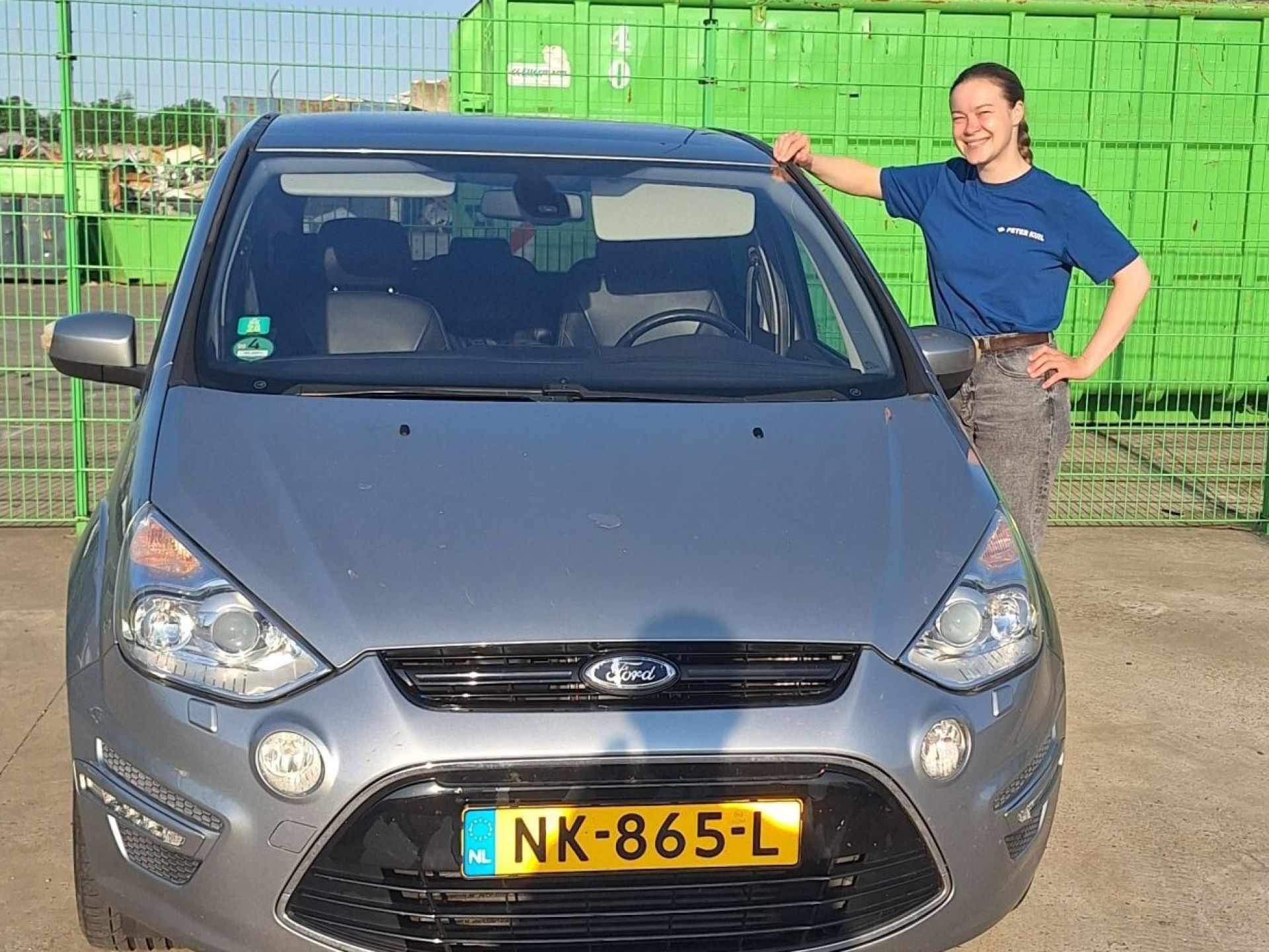 Vrouw naast een grijze auto met Nederlands kenteken.